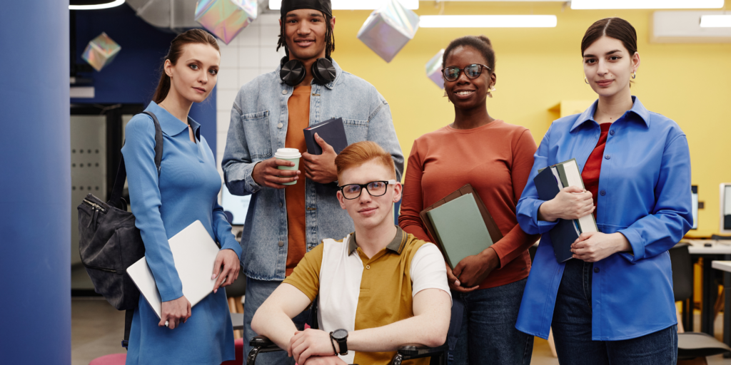 Group of 5 young adults holding either a book or laptop in a work environment setting 