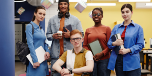 Group of 5 young adults holding either a book or laptop in a work environment setting