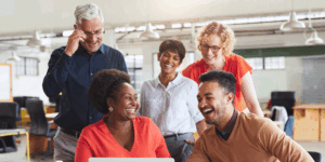 a group of people in an office looking at a laptop and laughing